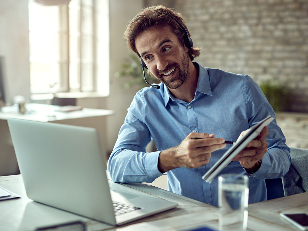 A smiling man wearing a headset is working on a laptop, showcasing a positive and engaged demeanor.