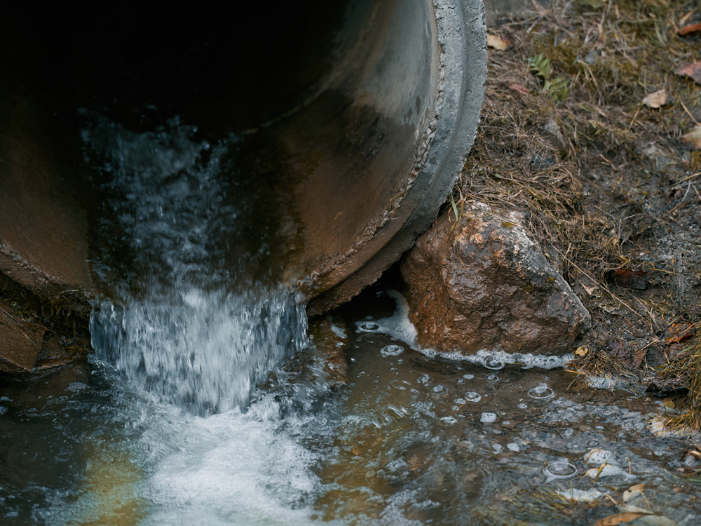 A pipe discharging a steady stream of water, illustrating fluid dynamics in a plumbing system.