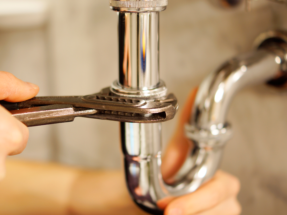 A person using a wrench to repair a pipe, demonstrating plumbing skills and maintenance work.