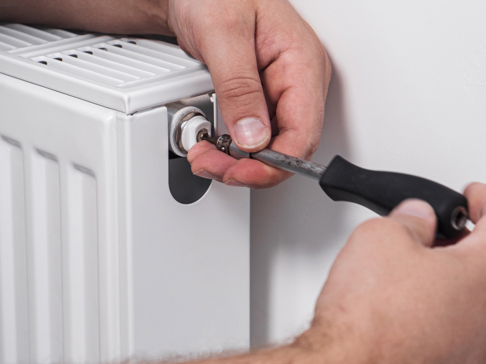 A person using a screwdriver to repair a radiator, demonstrating hands-on maintenance skills in a home setting
